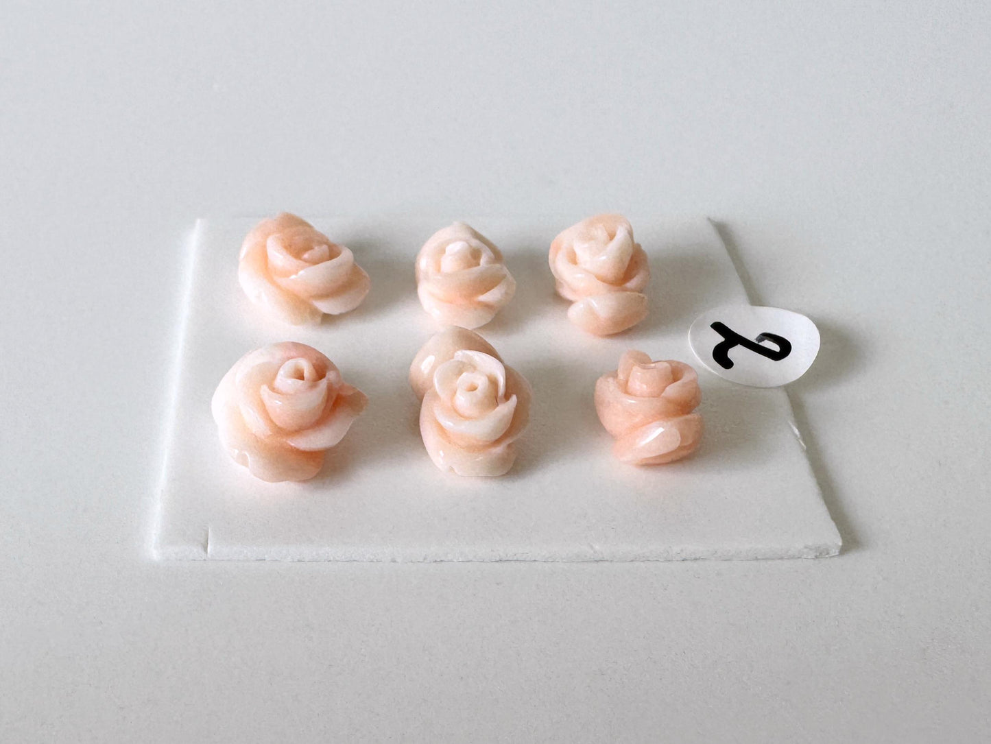 six pink rose-shaped objects arranged on a white surface.