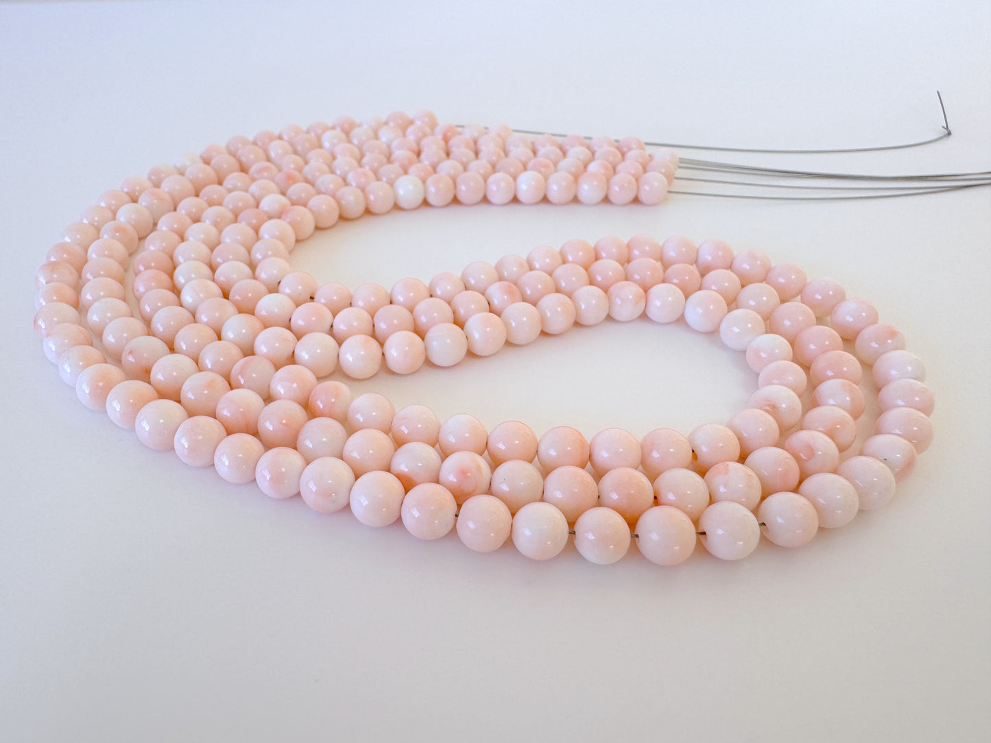 A long, delicate necklace made of small, round, pink beads arranged in a curved pattern.