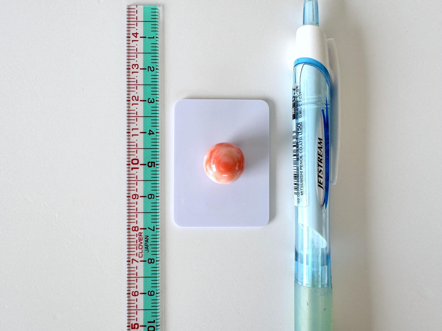 a ruler, a small orange object, and a blue pen on a white surface.