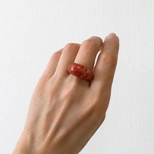 A hand wearing a red ring is shown against a white background.
