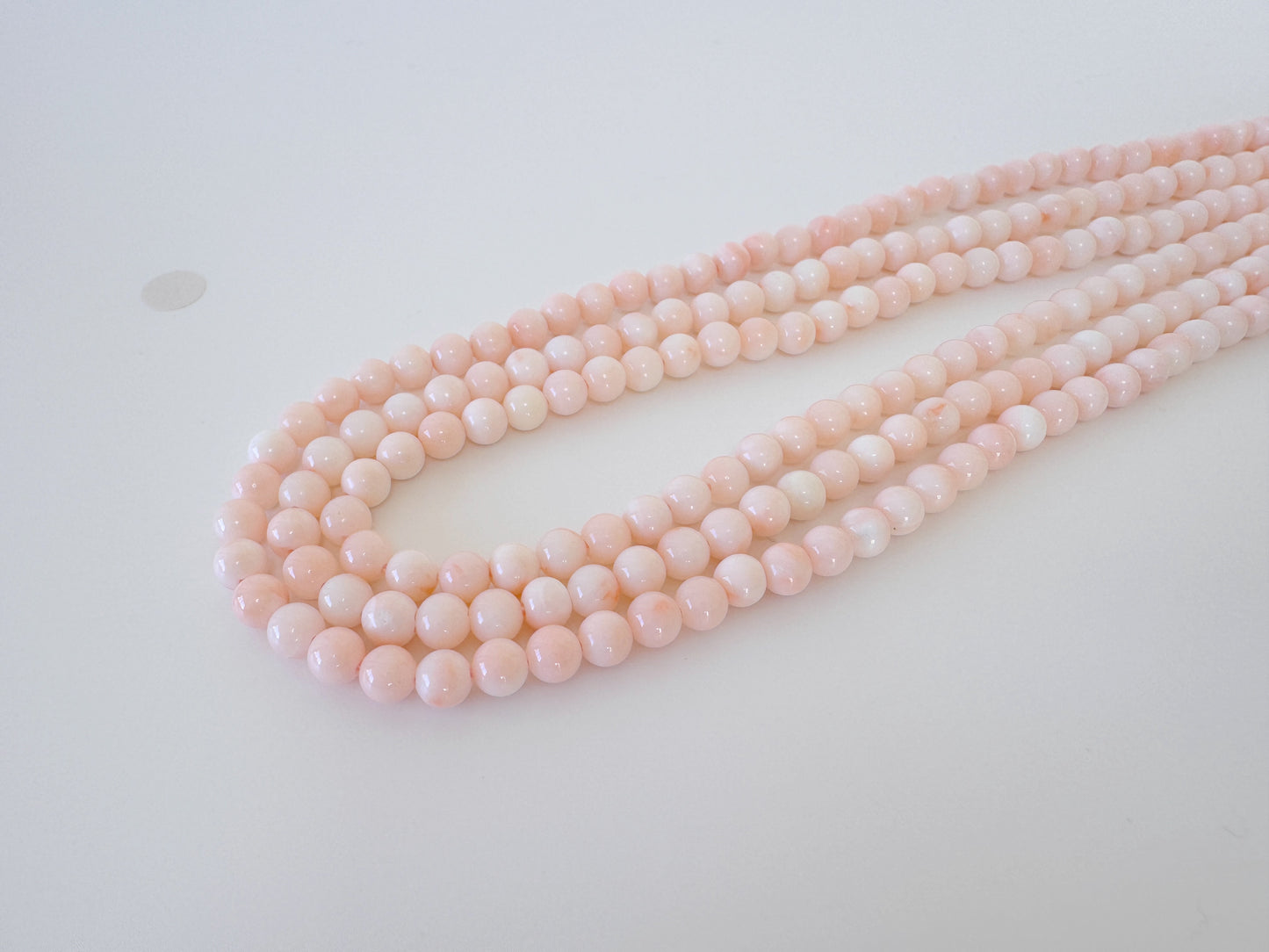 A necklace of pink beads arranged in a curved pattern on a white surface.