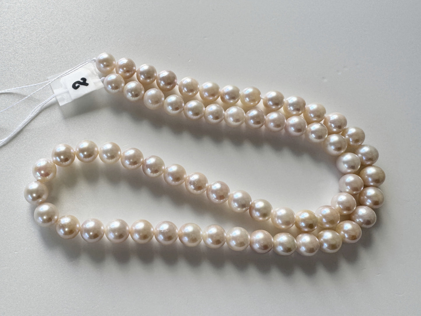 A necklace made of small, round, white pearls is displayed on a white surface.