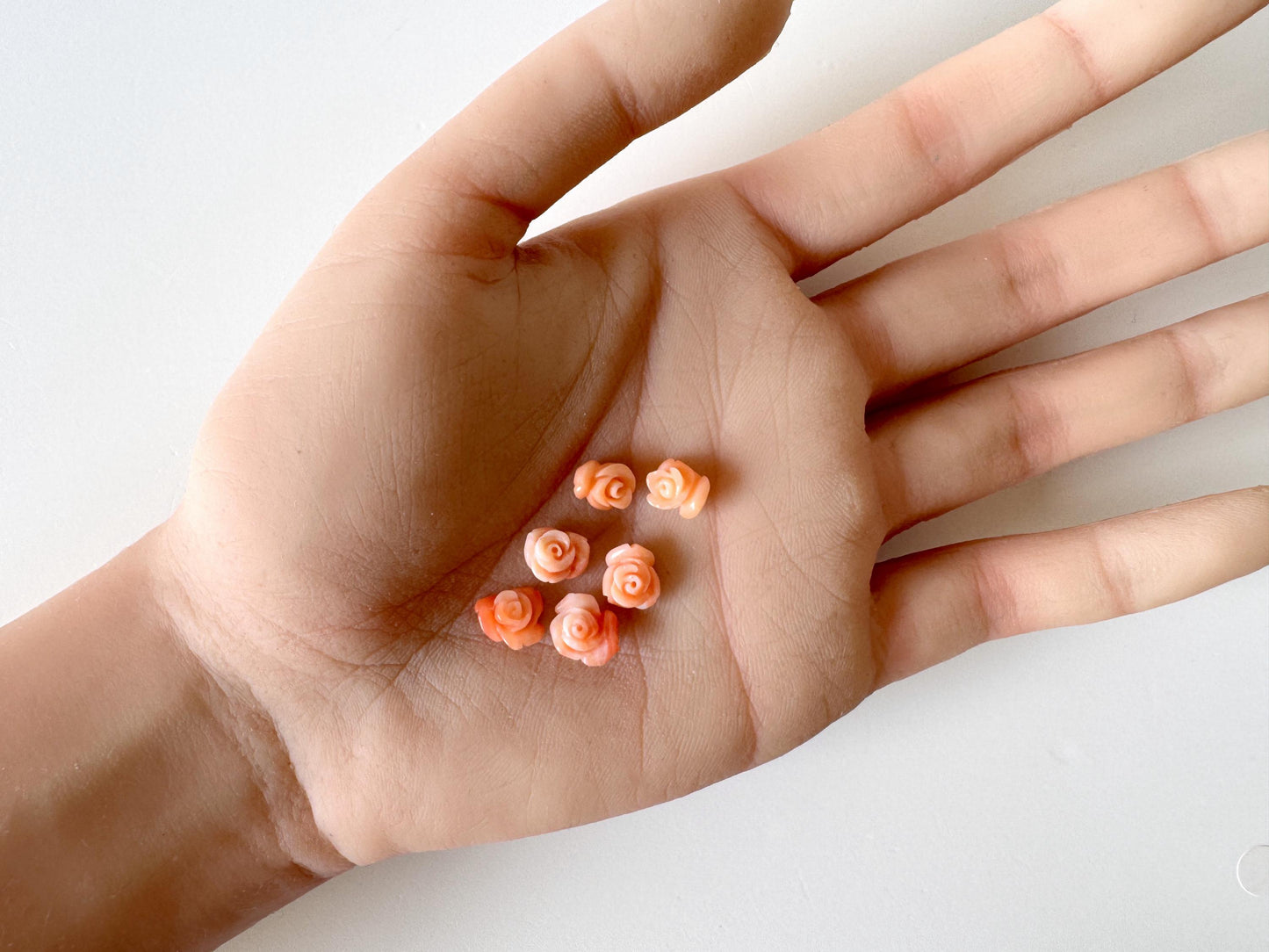 A hand holding a small group of orange flower-shaped objects, which appear to be tiny beads or decorations.