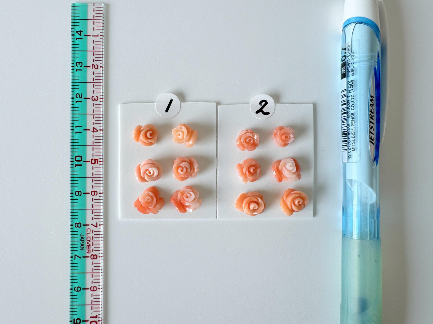 a collection of small orange rose-shaped objects, a ruler, and a pen, all arranged on a white surface.
