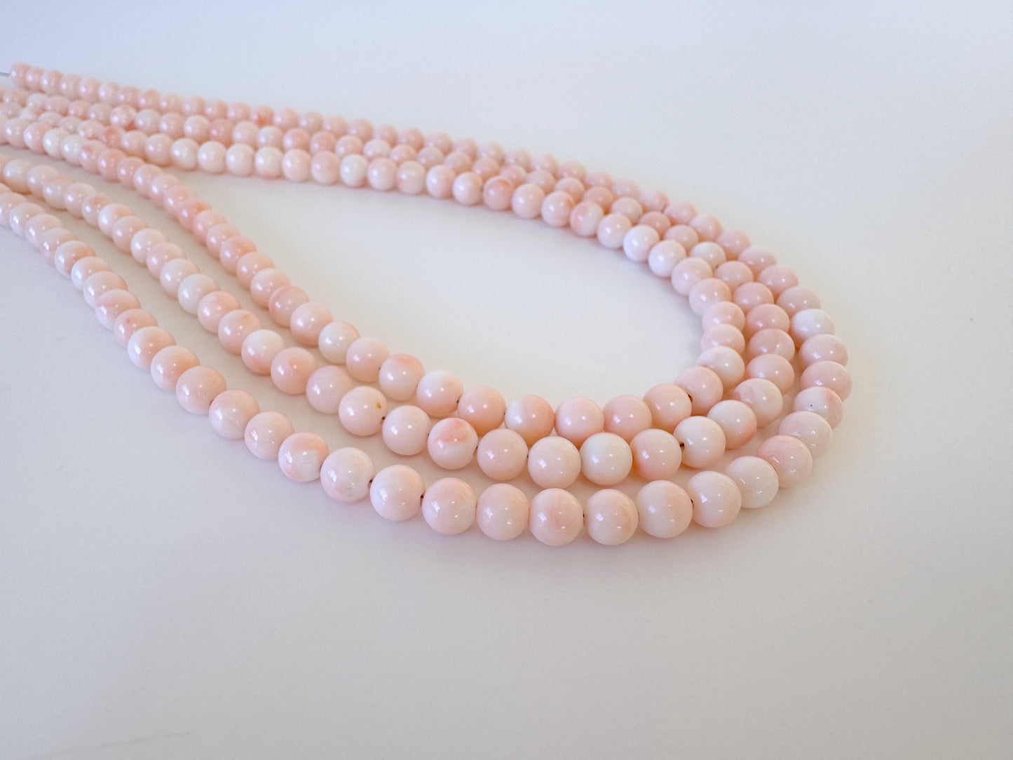 A close-up image of a necklace composed of numerous small, round, pink beads arranged in a curved pattern.