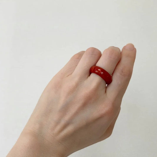 A hand wearing a red ring is shown against a plain white background.