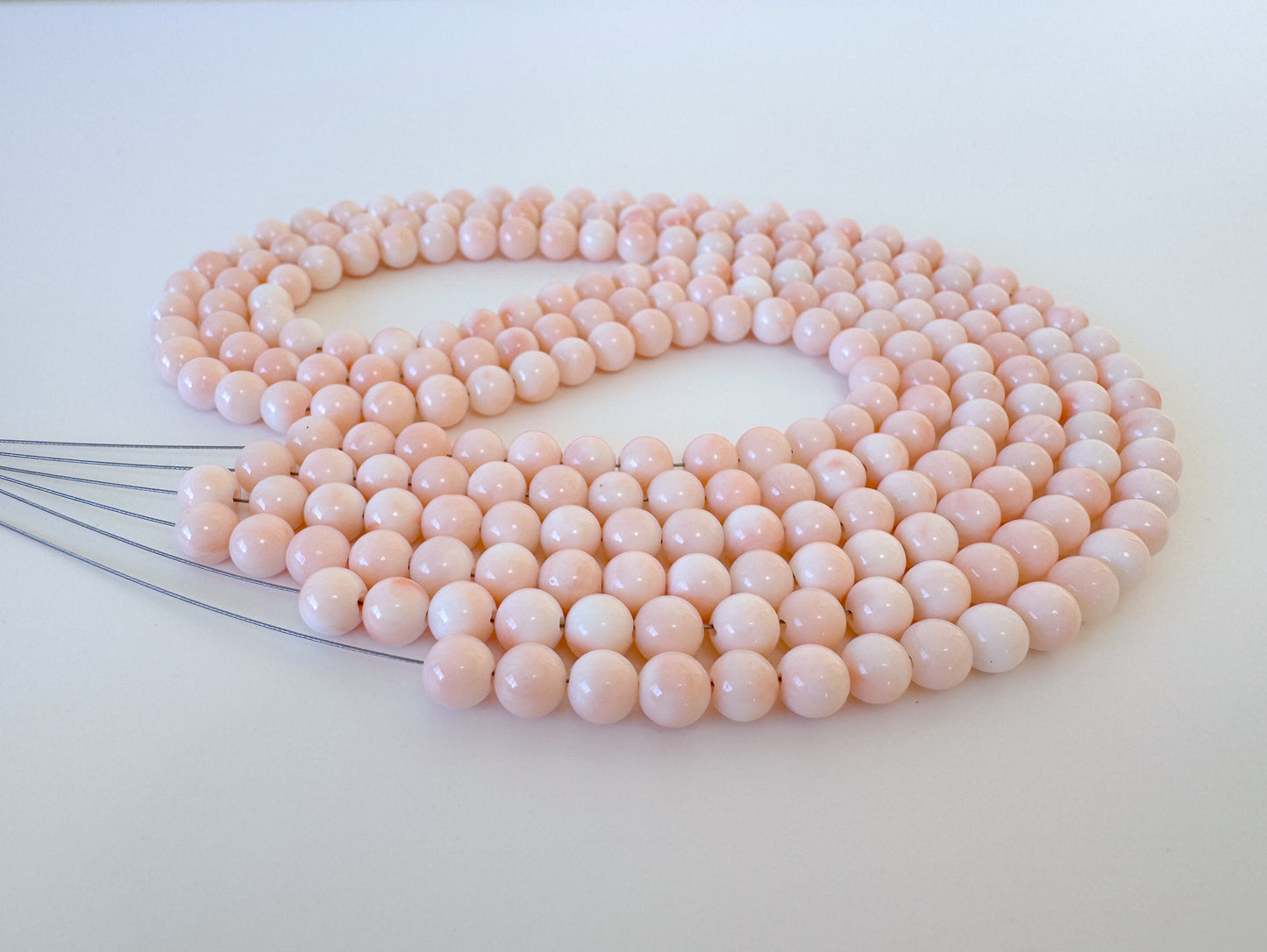 A necklace composed of numerous small, round beads in a light pink color, arranged in a circular pattern.