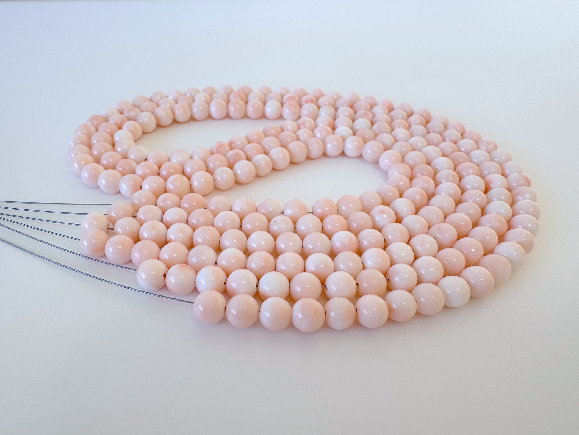 A necklace composed of numerous small, round beads in a light pink color, arranged in a circular pattern.