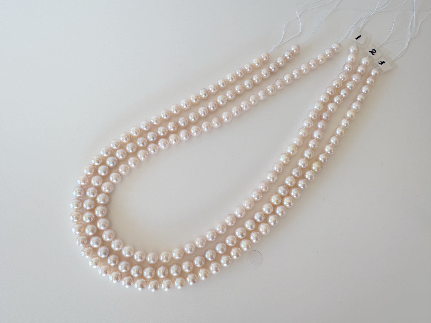 A necklace composed of three strands of white pearls is displayed on a white surface.
