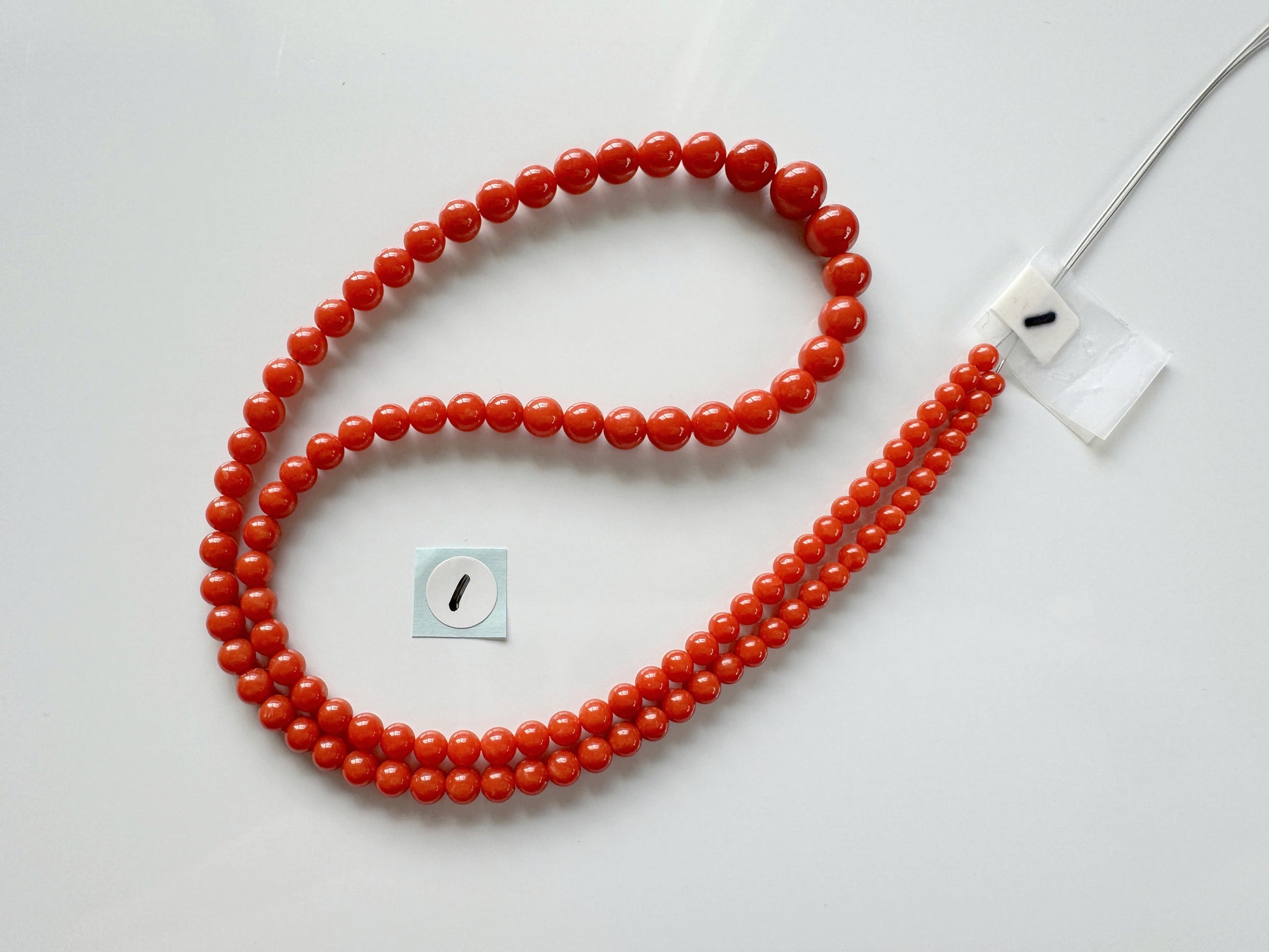 a red beaded necklace with a white tag attached to it